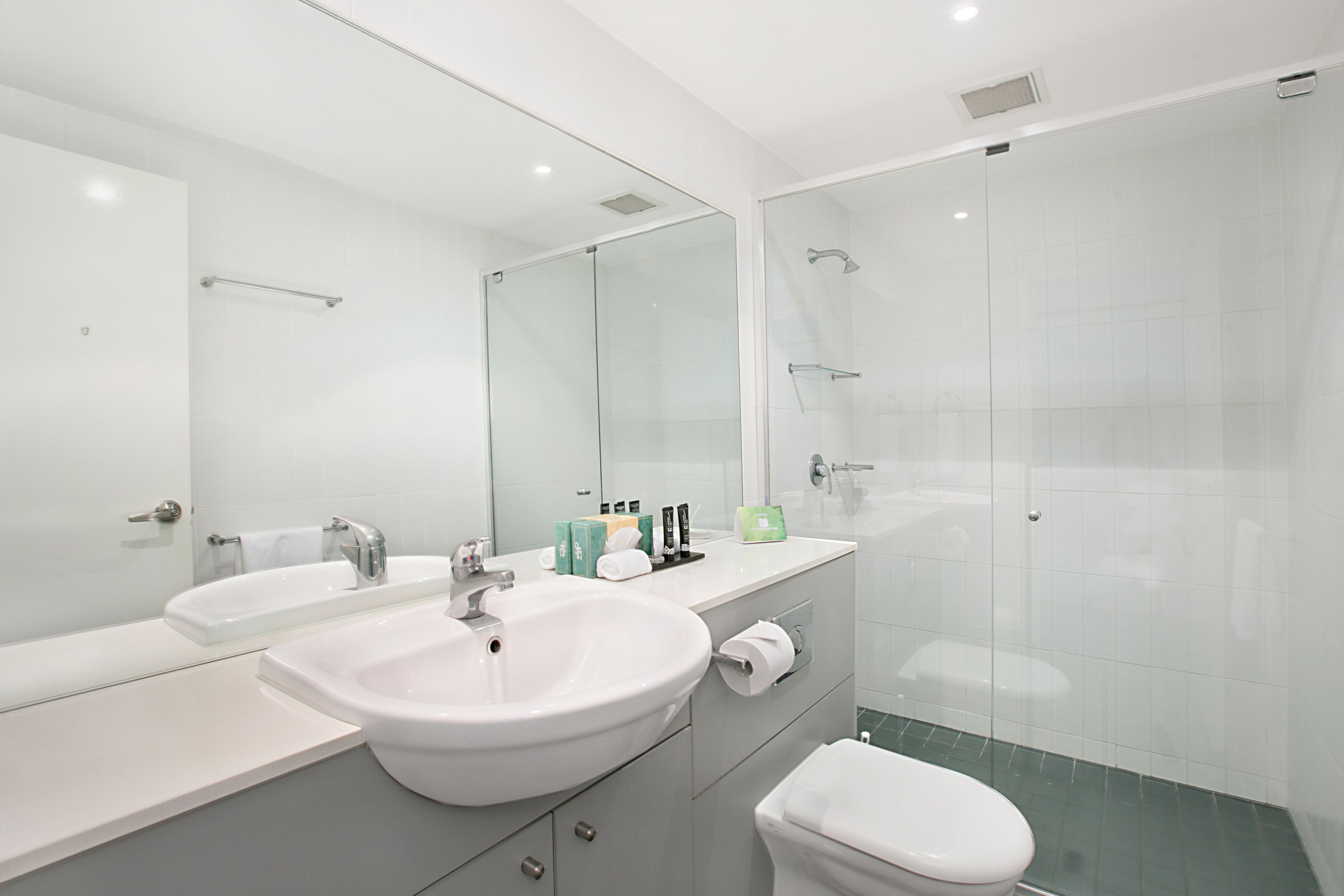 A modern bathroom with two sinks, a toilet, and a glass shower enclosure.