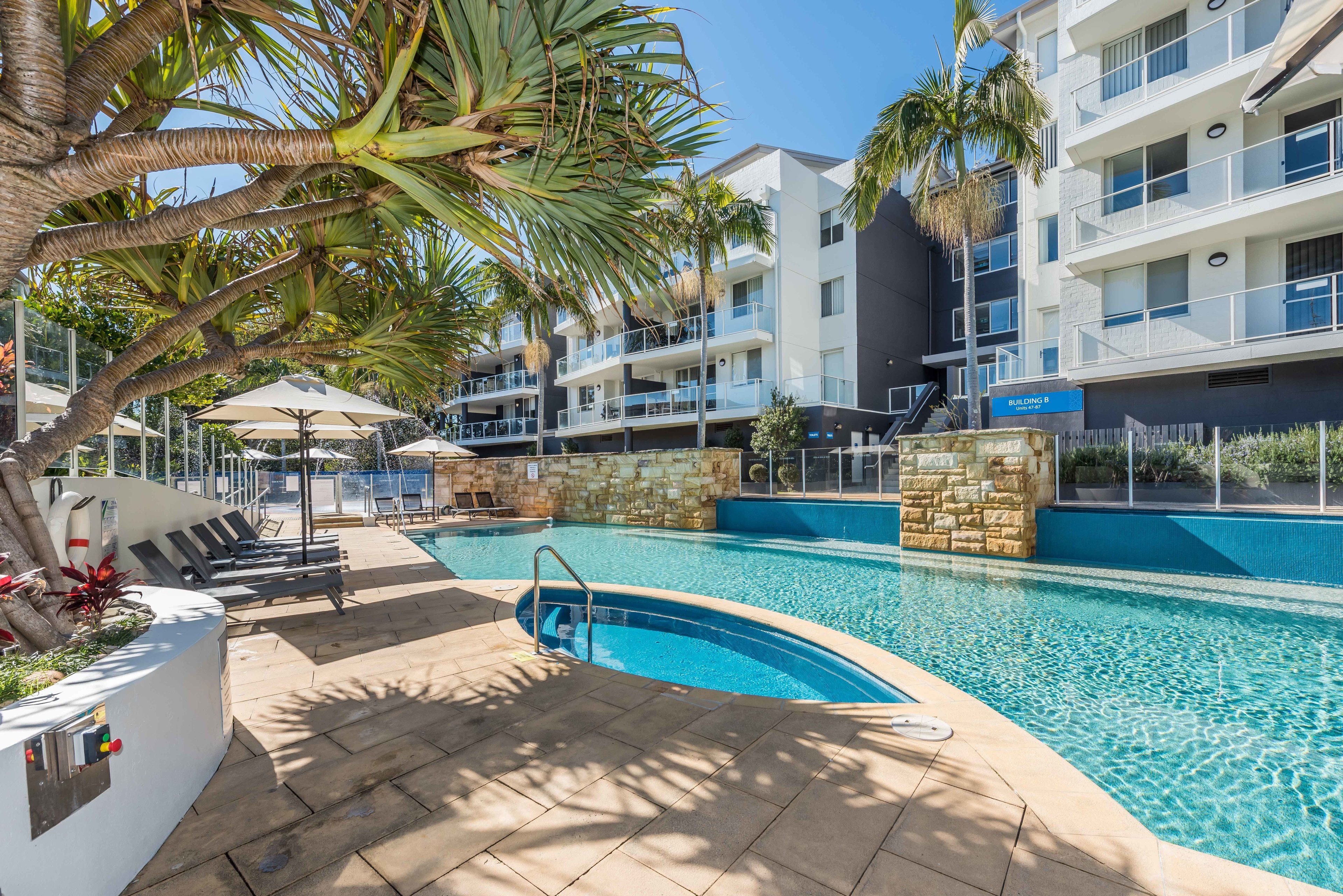 A swimming pool area with lounge chairs, umbrellas, and a stone wall.