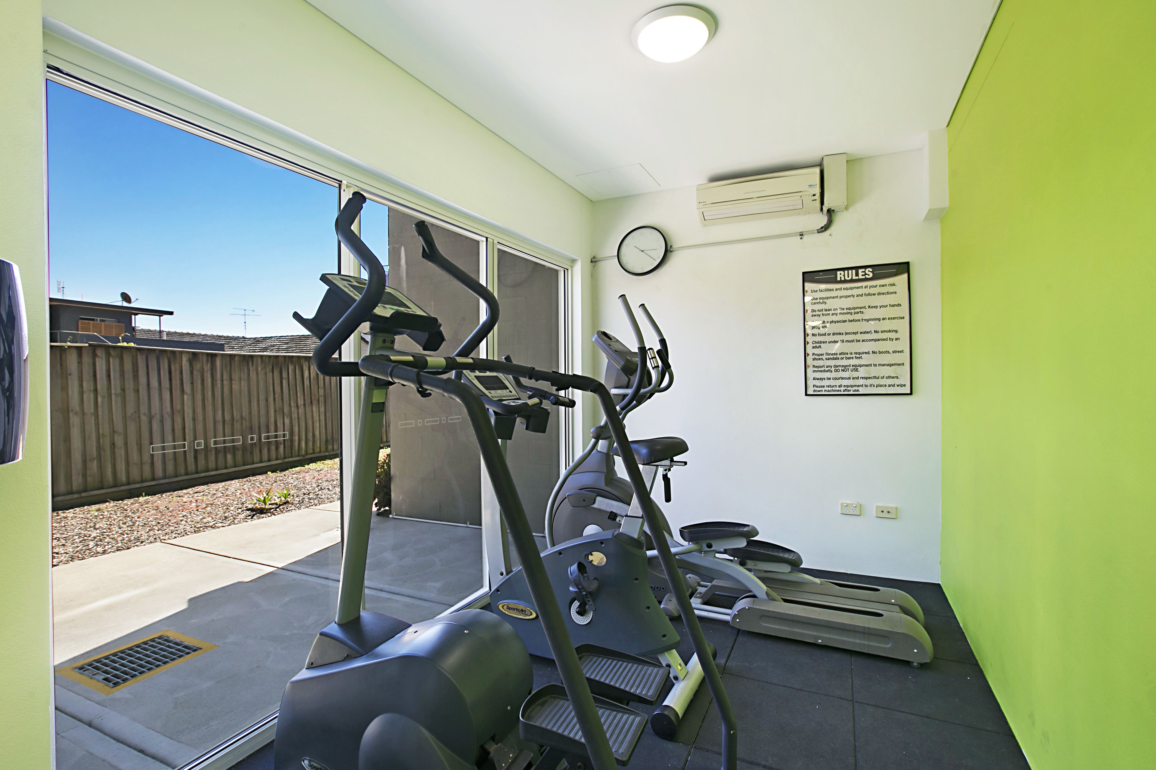 Un gimnasio con cintas de correr, elíptica y un reloj en la pared.