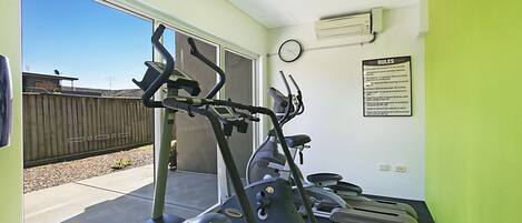 Un gimnasio con cintas de correr, elíptica y un reloj en la pared.