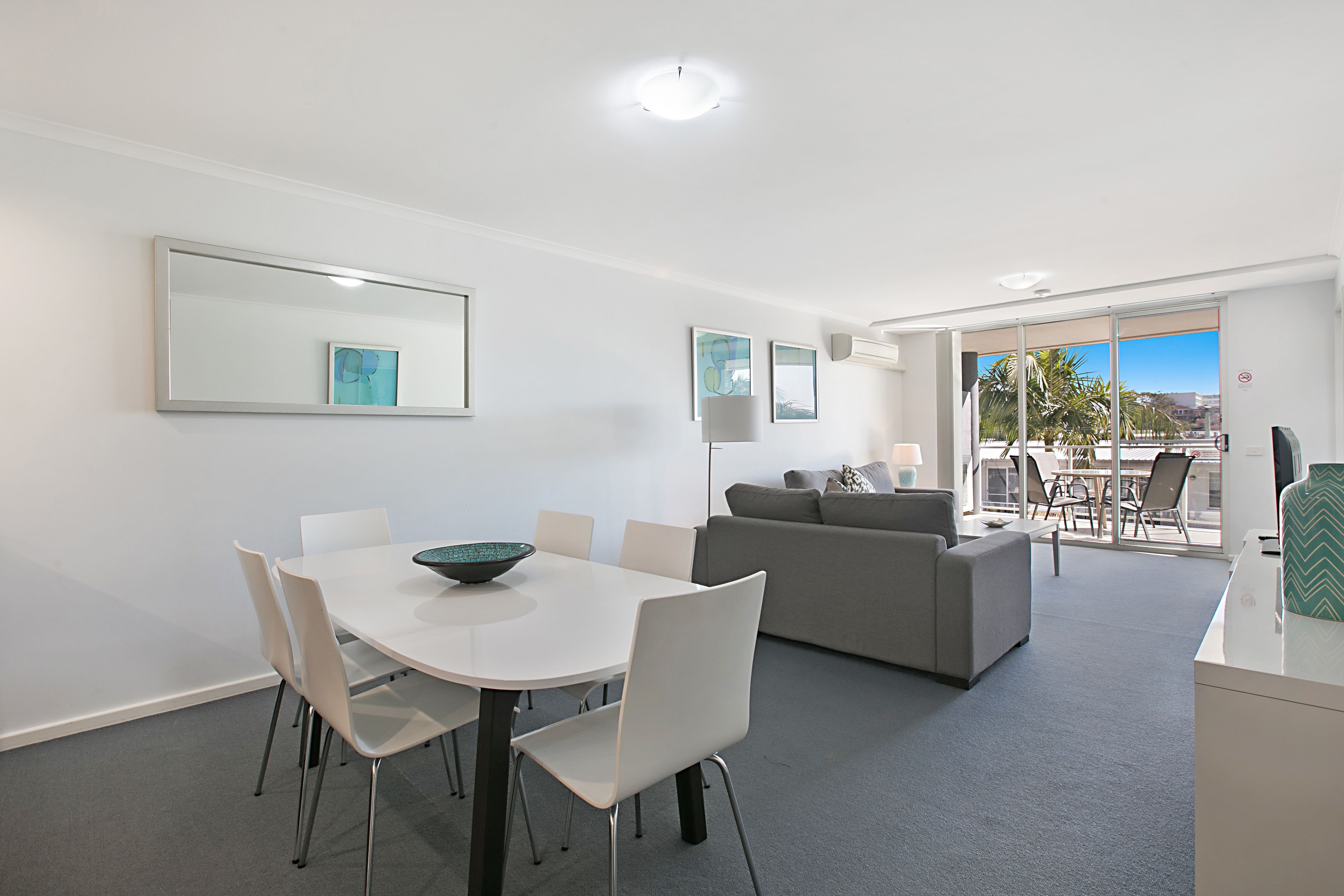 A modern hotel room with a dining area, a sofa, and a balcony with a view.