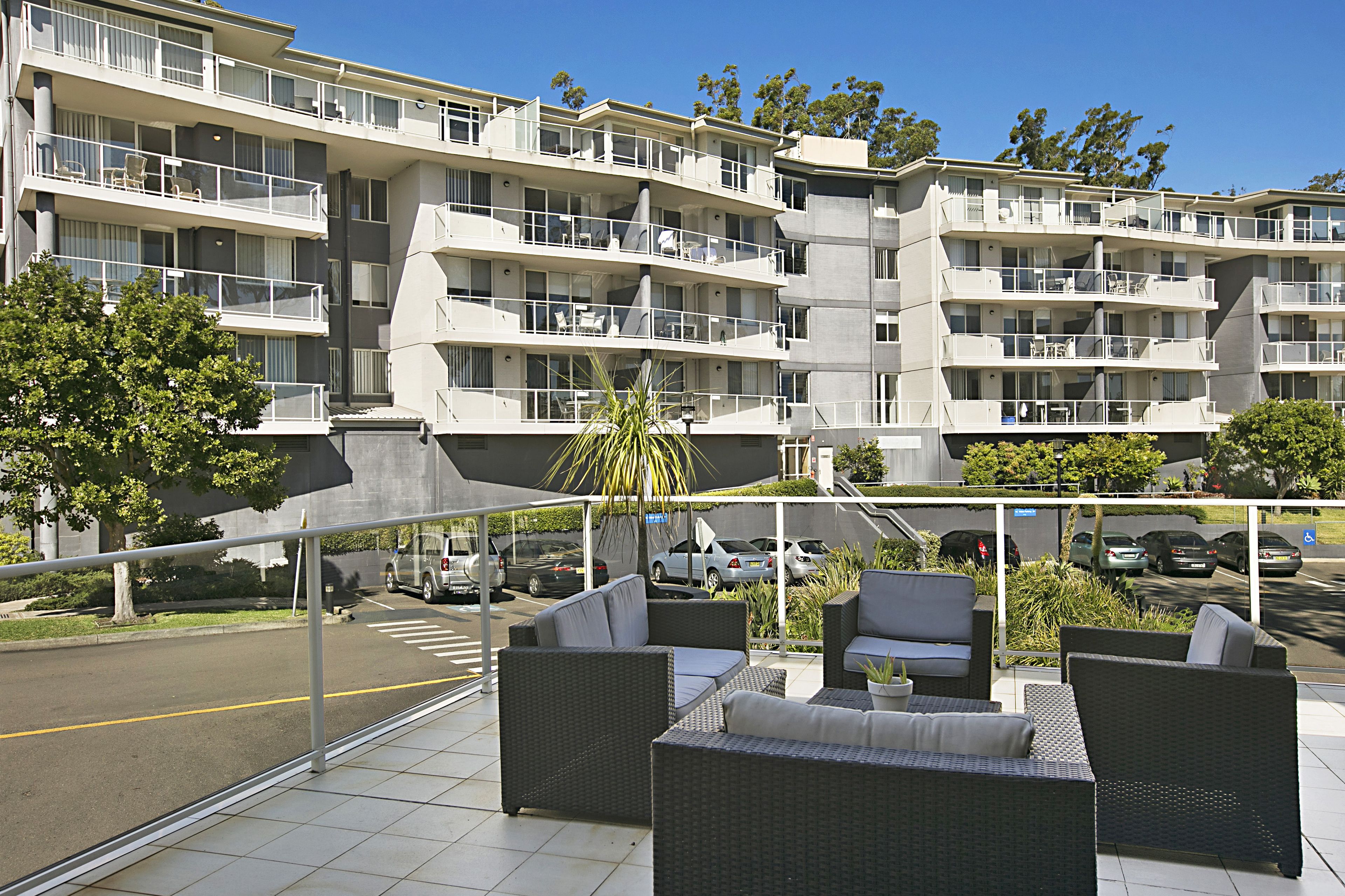 Un edificio residencial de varios pisos con balcones, mobiliario exterior y una zona de estacionamiento.