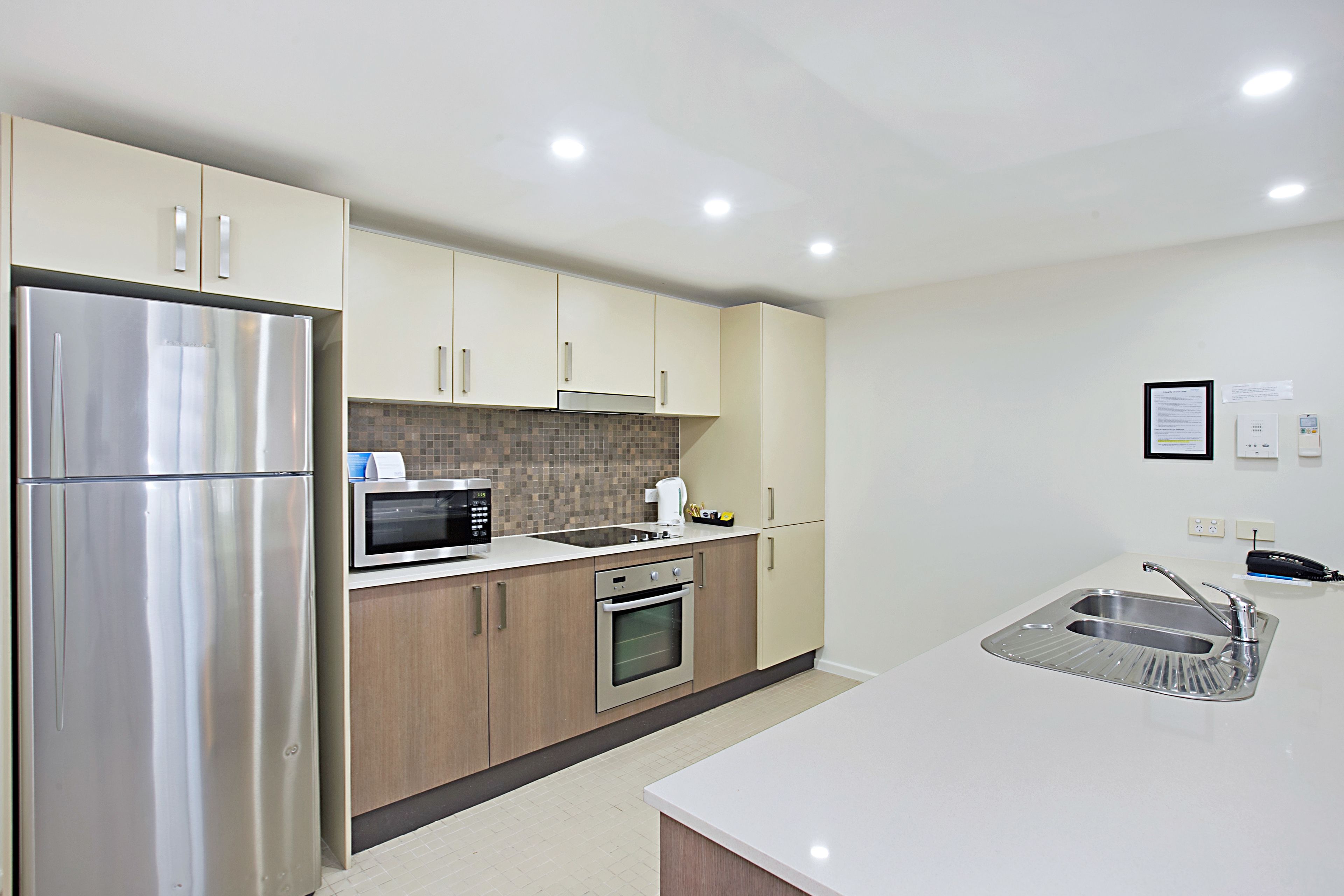Una cocina moderna con electrodomésticos de acero inoxidable, armarios de madera y una encimera blanca.