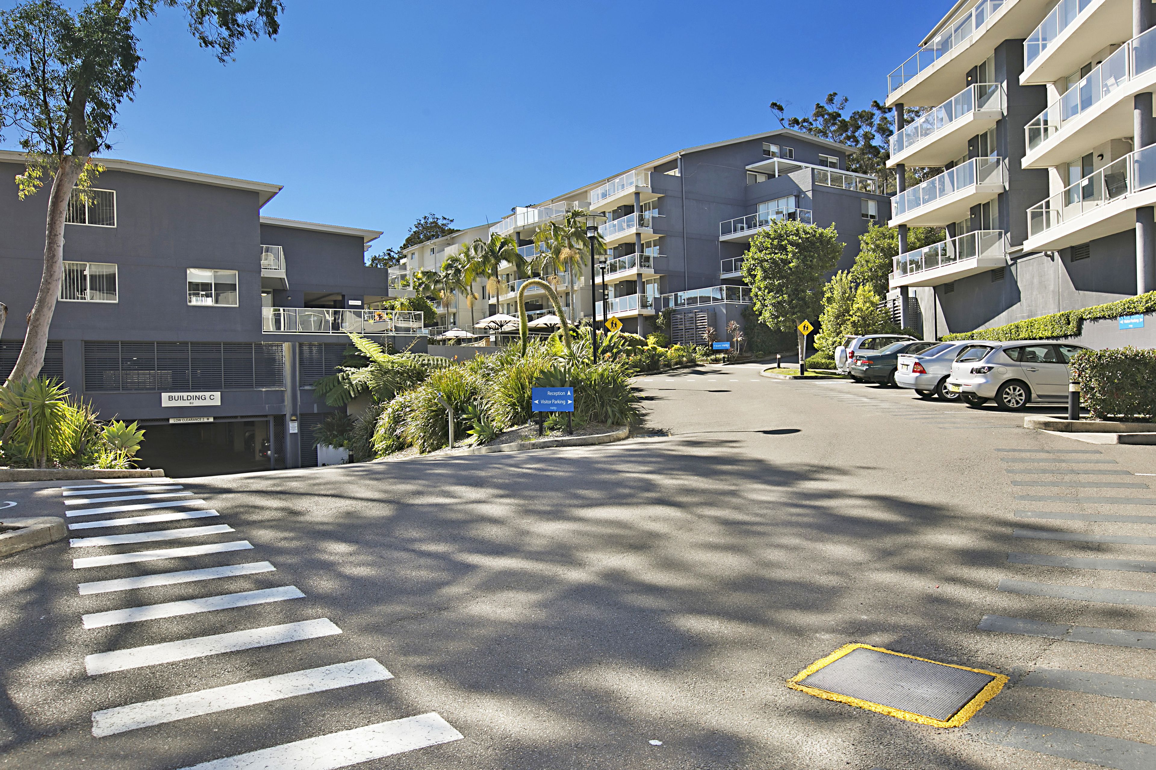 A multi-story residential building with balconies, a pedestrian crossing, and parked cars.