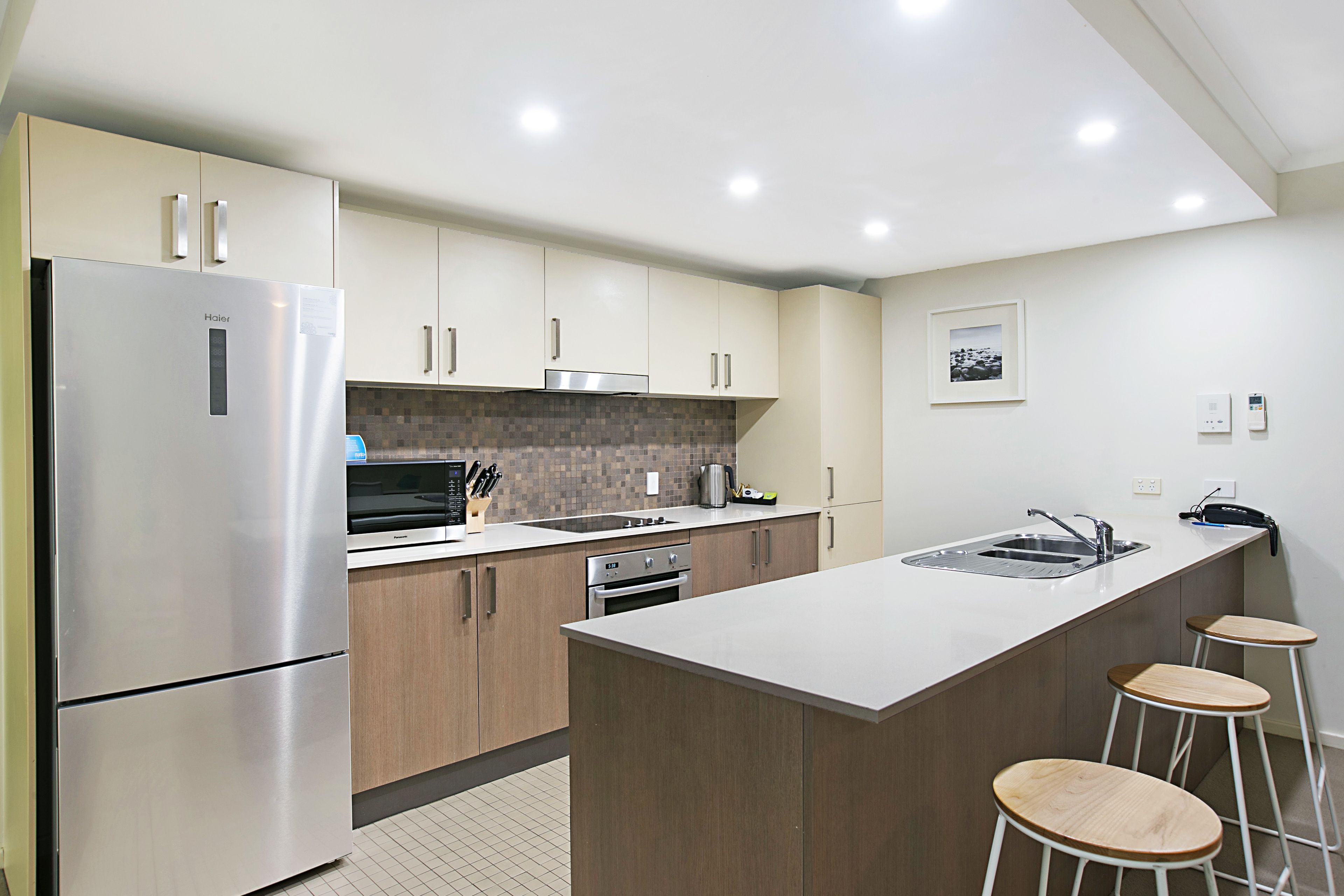 A modern kitchen with stainless steel appliances, wooden cabinets, a tiled backsplash, and a bar area with stools.