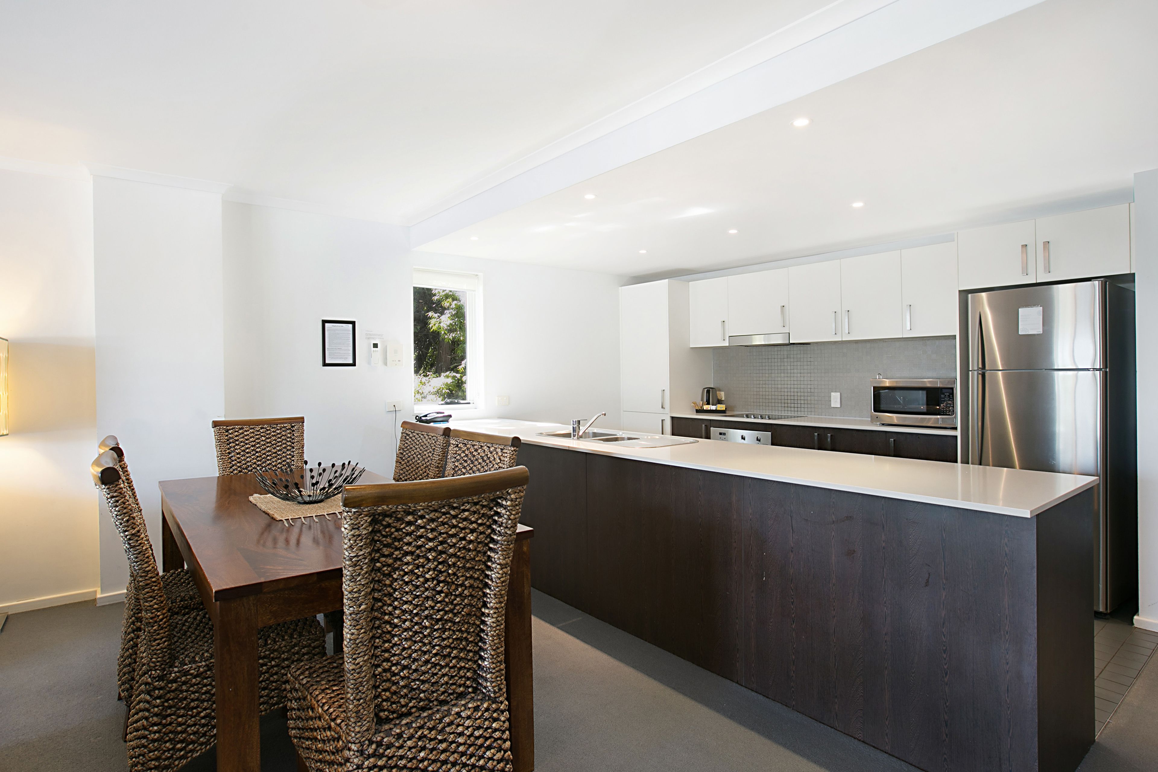 A modern kitchen with a central island, stainless steel appliances, and a dining area with wicker chairs.