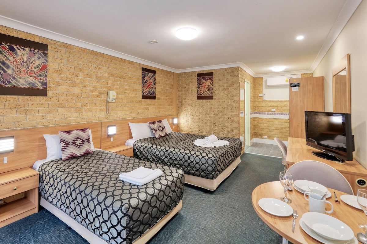A hotel room with two beds, a desk with dining set, a TV, and artwork on the walls.