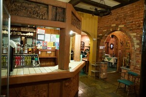 Un’area bar con scaffali in legno che espongono bottiglie e bicchieri, un muro in mattoni con decorazioni e un’area salotto con tavoli e sedie.
