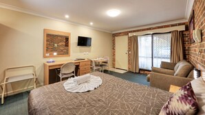 Ett hotellrum med en säng, ett skrivbord, en stol, en soffa, en TV och en skjutdörr av glas.