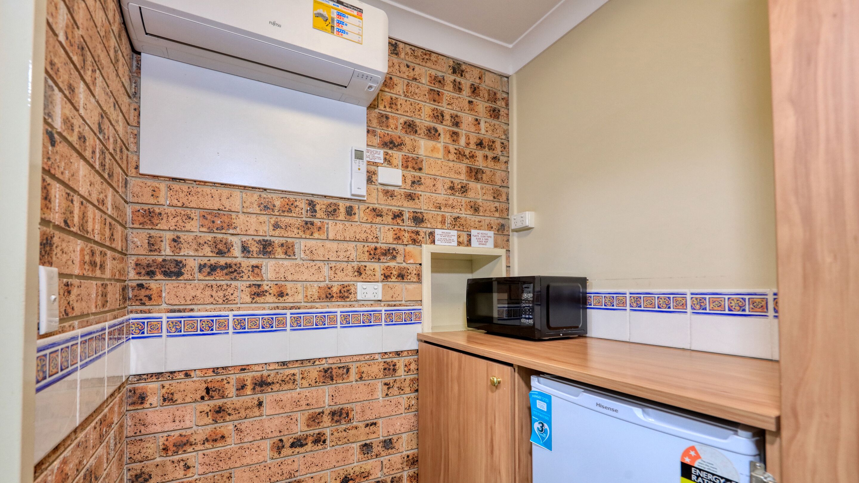 A compact kitchen with a brick backsplash, a microwave, and a small refrigerator.