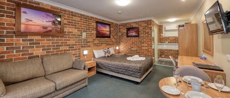 A hotel room with a brick wall, a bed with a quilt, a sofa, a dining table set with plates and glasses, and a TV mounted on the wall.