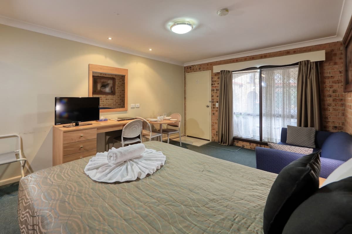 A hotel room with a bed, a desk with a computer, a chair, a TV, and a window with curtains.