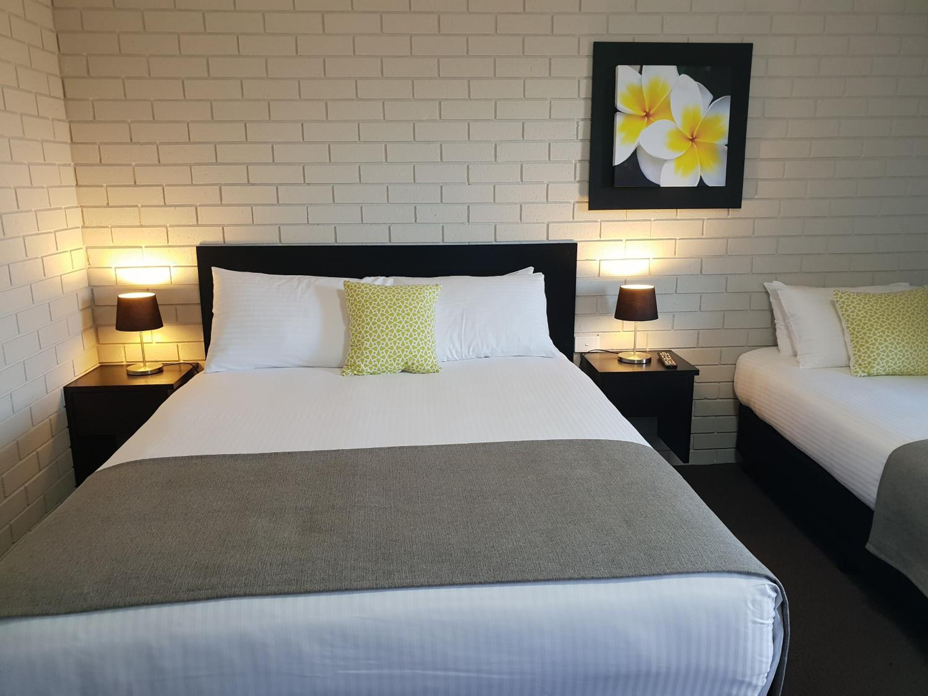 Una habitación de hotel con una cama grande, dos mesitas de noche con lámparas, un tocador y un cuadro de flores colgado en la pared.