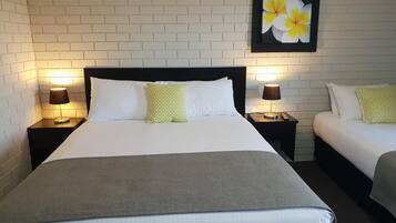 Una habitación de hotel con una cama grande, dos mesitas de noche con lámparas, un tocador y un cuadro de flores colgado en la pared.