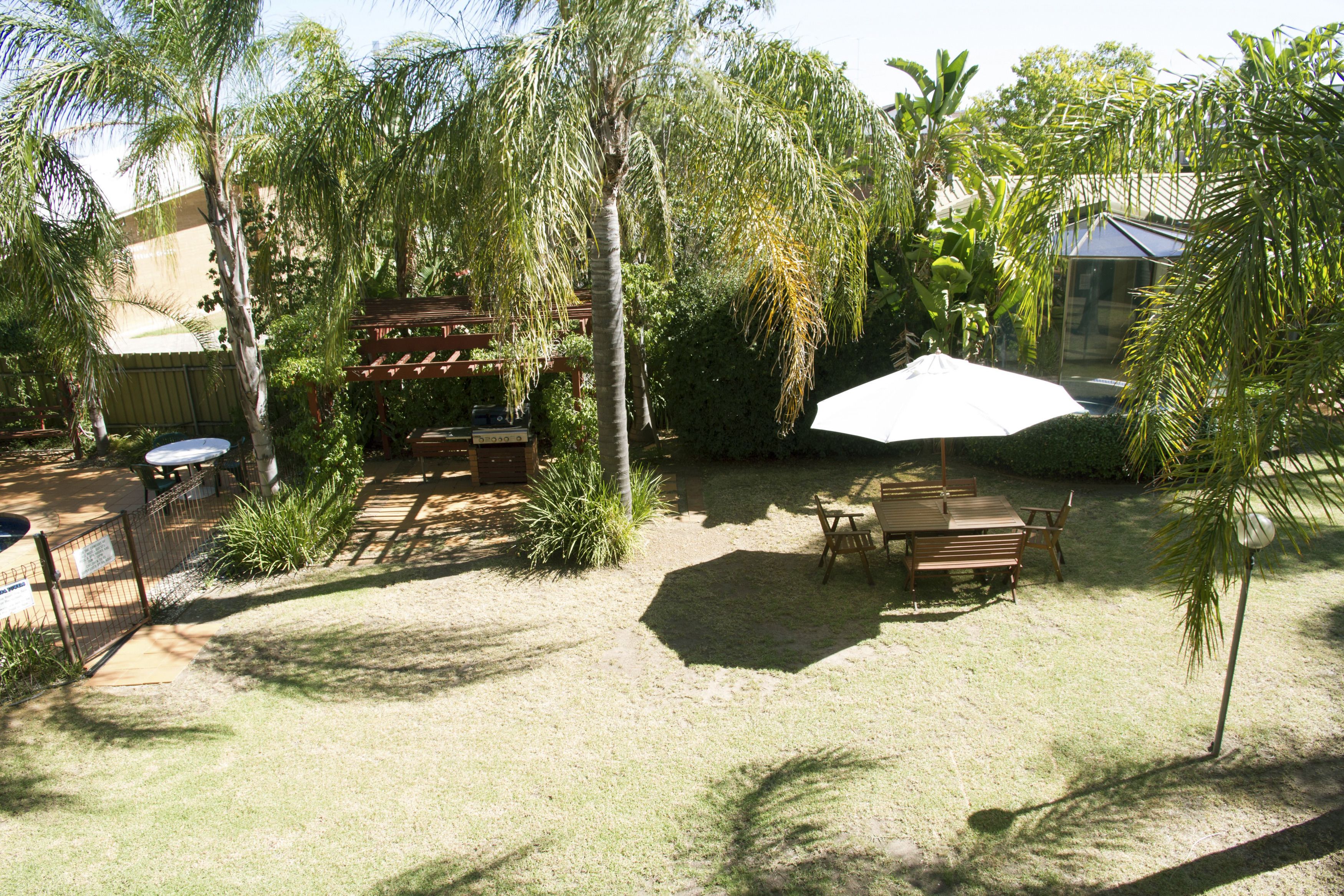 A backyard with a wooden table and chairs, a white umbrella, and palm trees.