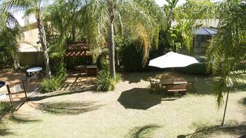 A backyard with a wooden table and chairs, a white umbrella, and palm trees.
