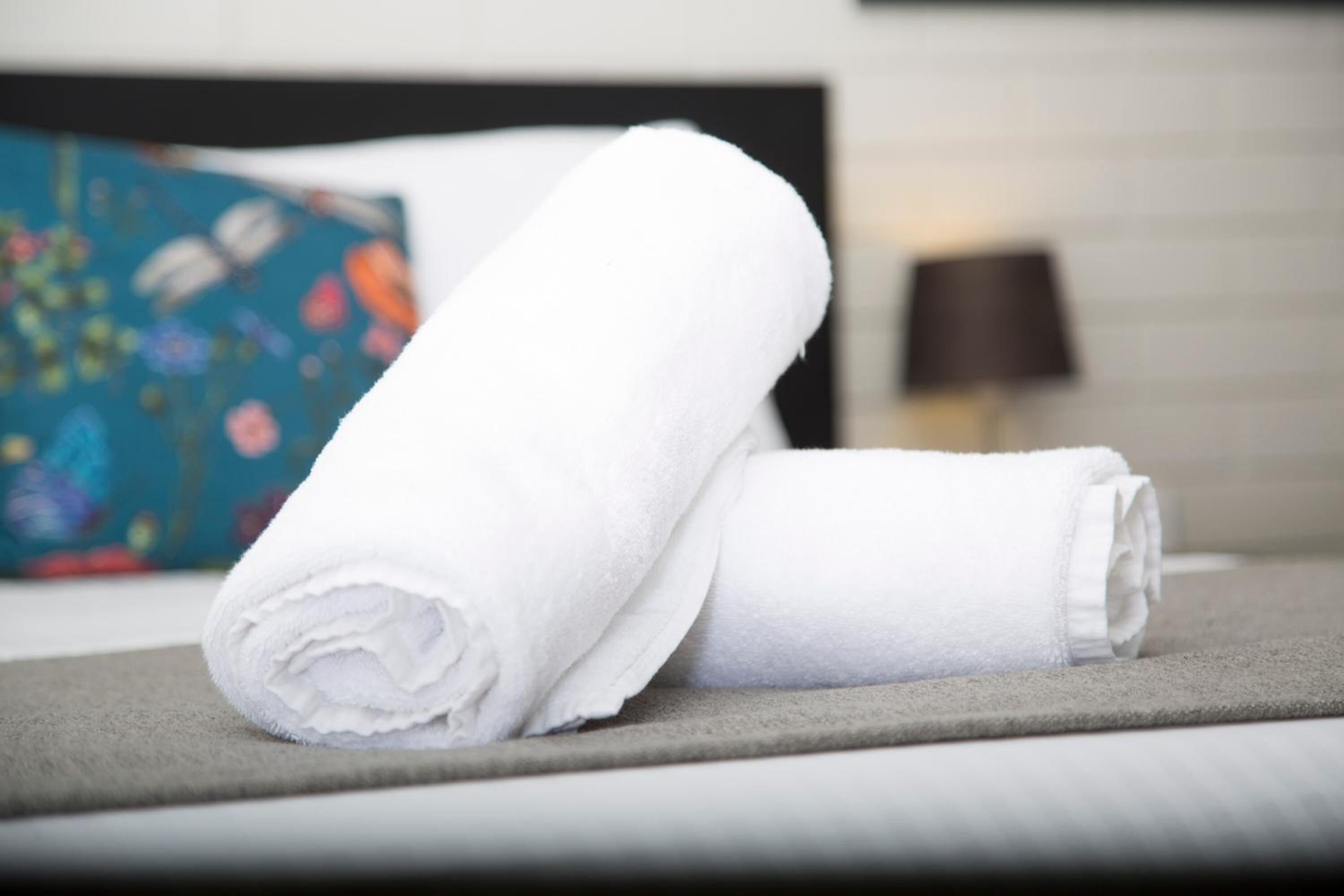 Siististi taitettu valkoinen pyyhe harmaalla alustalla hotellihuoneessa.