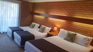 A hotel room with three beds, a brick wall, a window with curtains, and a nightstand with a lamp. - Crystal Fountain Motel Albury (Lavington)