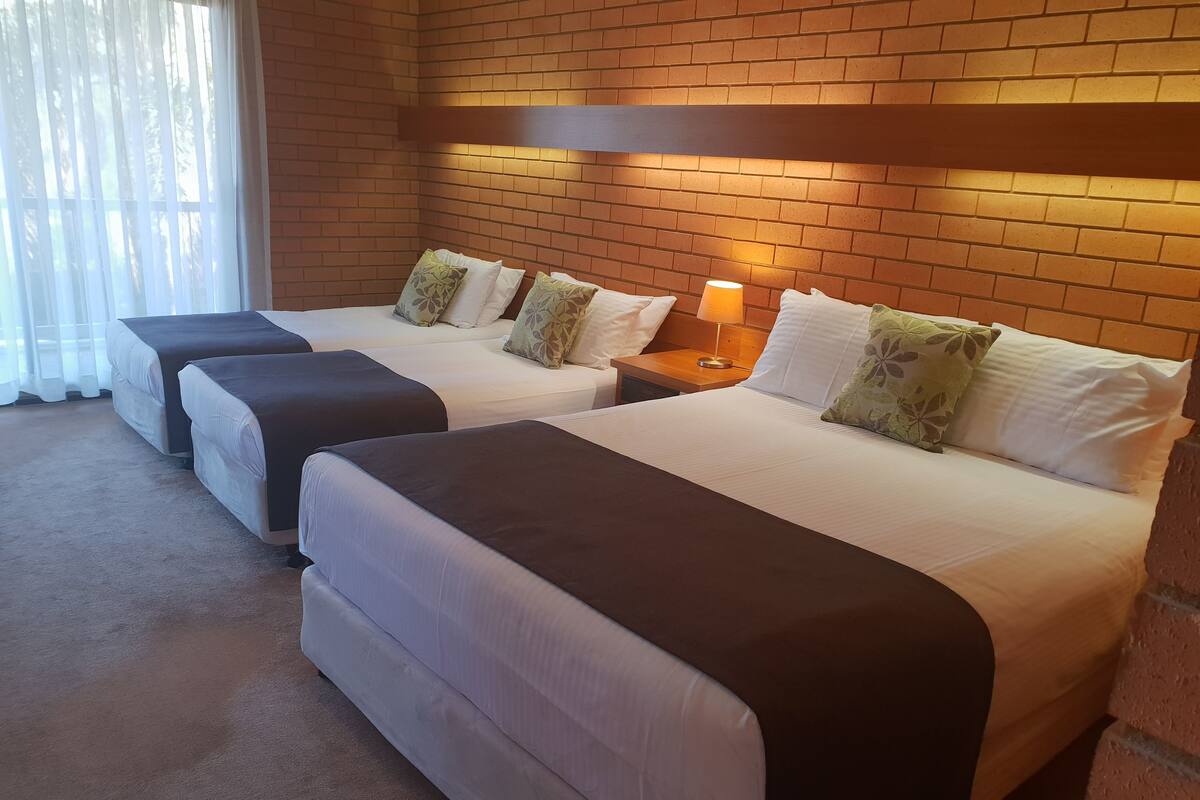 A hotel room with two beds, each with a headboard, a nightstand with a lamp, and a brick wall.