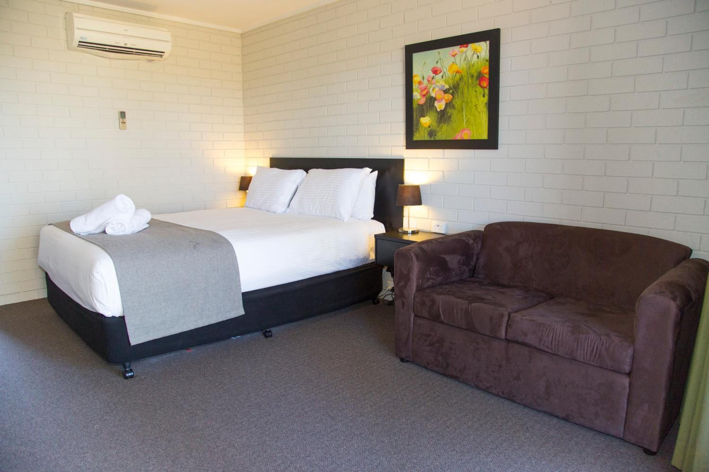 Une chambre d’hôtel avec un lit, un canapé marron, un appareil de climatisation et un tableau au mur.