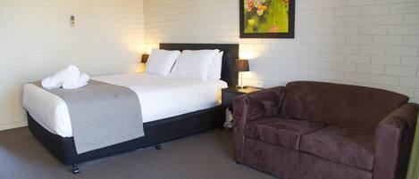 Une chambre d’hôtel avec un lit, un canapé marron, un appareil de climatisation et un tableau au mur.