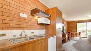 A compact kitchen with a sink, stove, and microwave. There's a dining area with a table and chairs. - Crystal Fountain Motel Albury (Lavington)