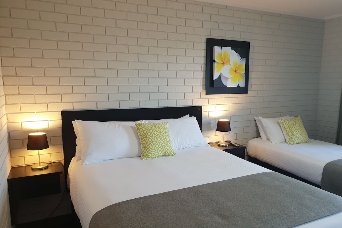 A hotel room with two beds, white bedding, and a brick wall.