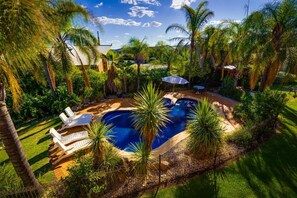 A swimming pool surrounded by lush greenery and palm trees, with a clear blue sky above. - Crystal Fountain Motel Albury (Lavington)