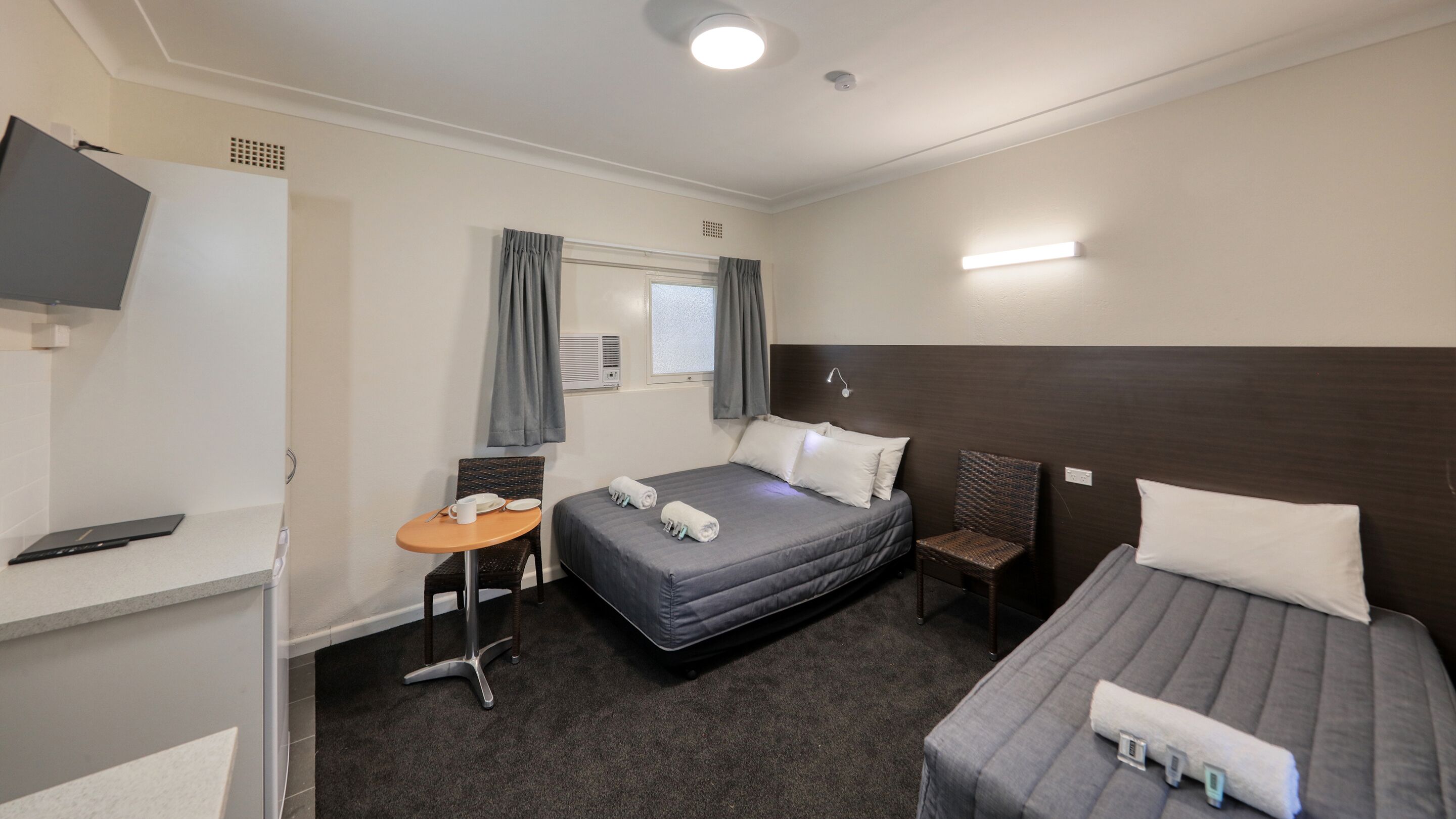 A hotel room with a bed, a smaller bed, a desk with a chair, a TV, and a window with curtains.