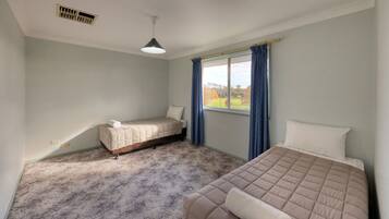 A bedroom with two beds, a window with curtains, a ceiling vent, and a light fixture.
