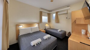 A hotel room with two beds, a desk, a chair, a television, and a window with curtains.