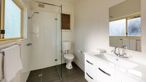 A bathroom with a glass shower enclosure, a toilet, a sink with a mirror, and a window.
