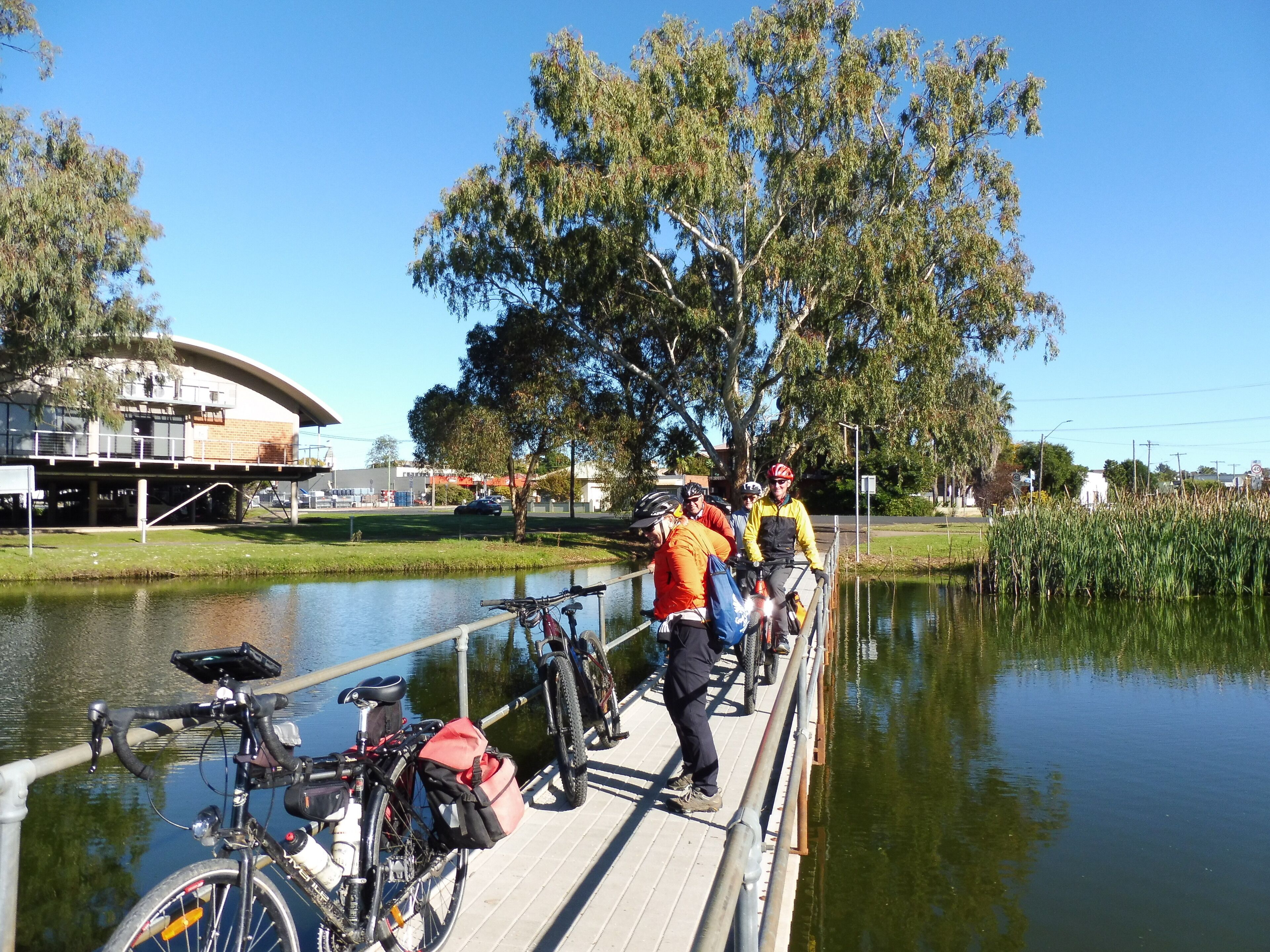 Un grupo de personas en un puente de madera sobre aguas tranquilas, con bicicletas estacionadas al lado.