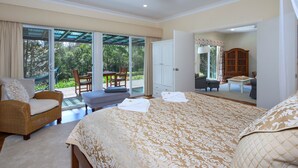 Een slaapkamer met een groot bed, een rieten stoel, een klein tafeltje en uitzicht op de omgeving via een schuifpui.