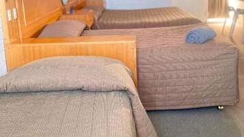 A hotel room with two beds, a wooden headboard, a small table, and a window with curtains.