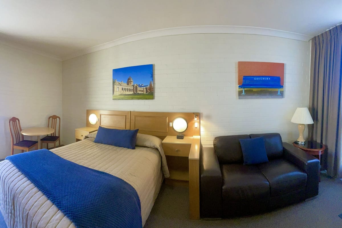 A hotel room with two beds, a sofa, a desk, and a lamp.