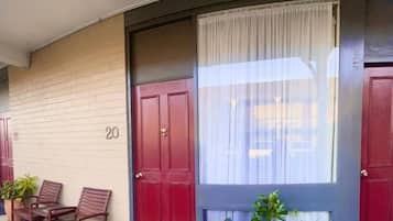 A building entrance with a red door, a window with a white curtain, and potted plants.