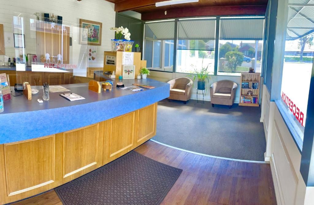 Een receptiebalie met een blauw aanrecht, houten kasten, een receptie, een stoel, een boekenkast en een groot raam.