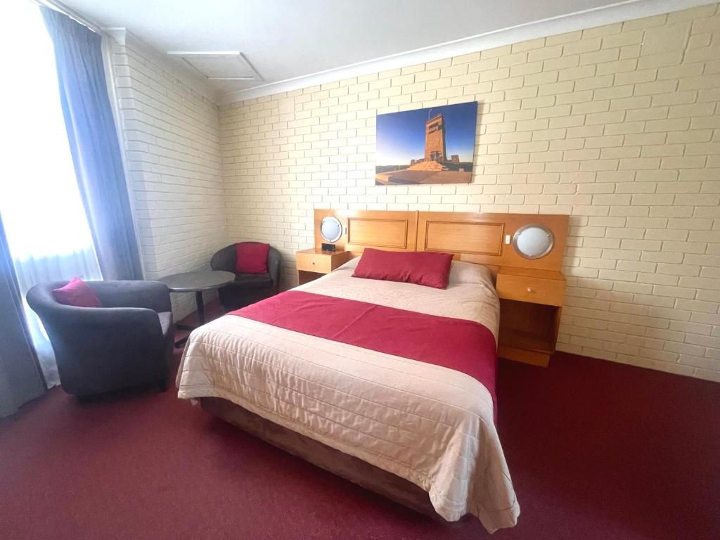 Et hotelværelse med en stor seng, et skrivebord, en stol og et billede på væggen.