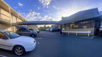 A parking area with multiple cars, a covered walkway, and a building with large windows.