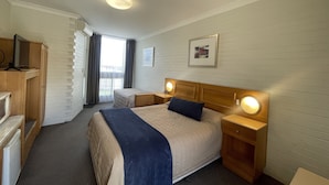 Une chambre d’hôtel comprenant un lit, des tables de chevet, un bureau, une armoire et une fenêtre avec des rideaux.