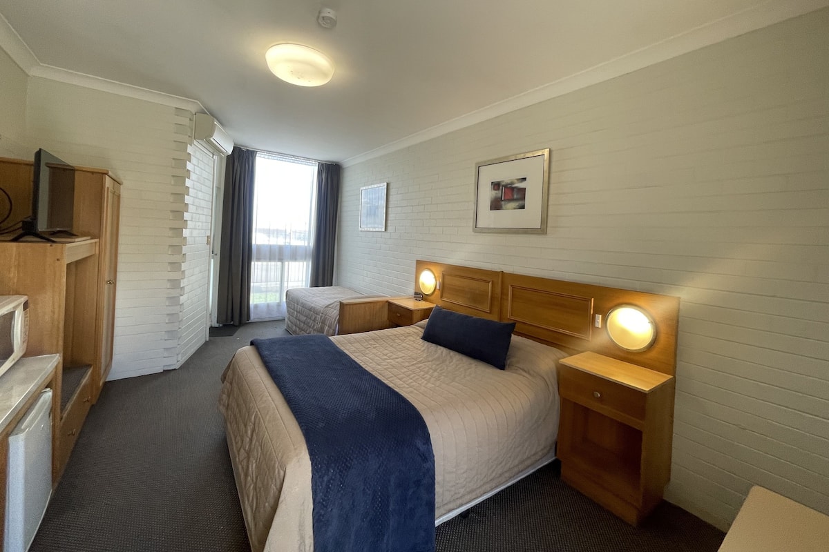 A hotel room with a bed, bedside tables, a desk, a wardrobe, and a window with curtains.