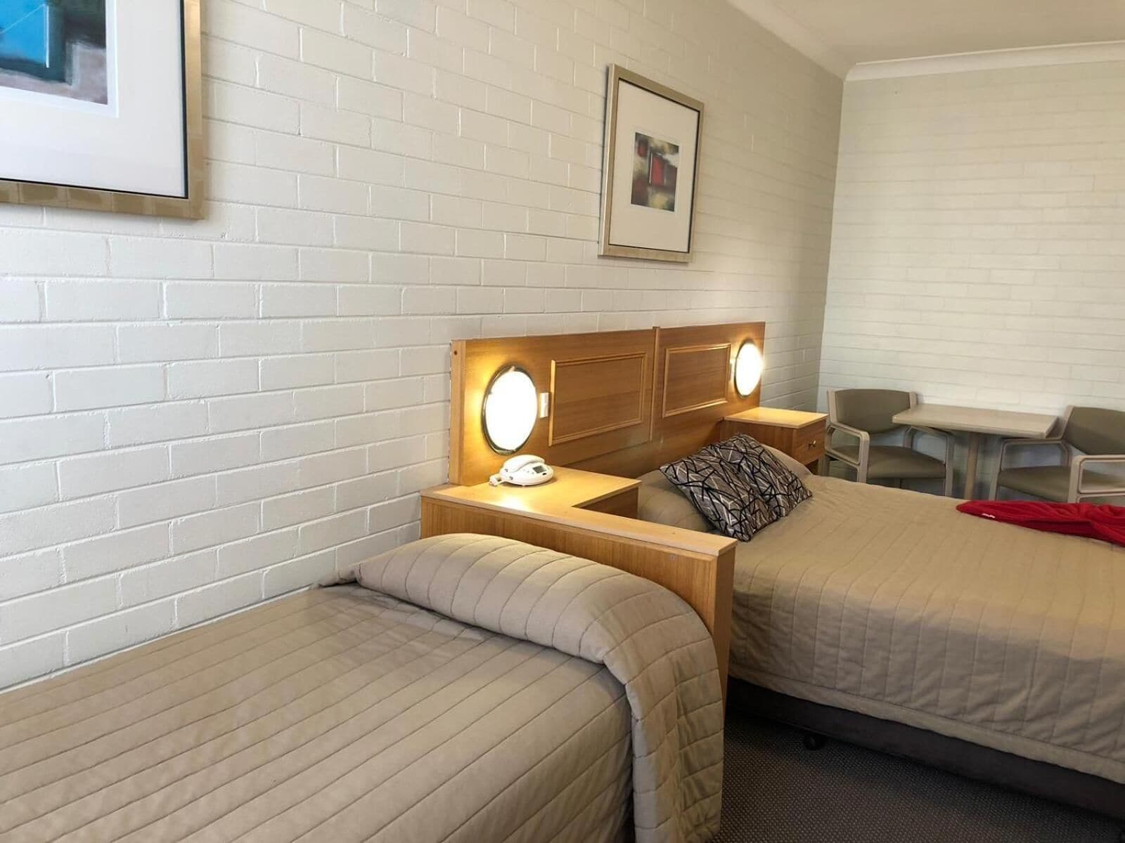 Ett hotellrum med två sängar, en sänggavel i trä med en spegel, sänglampor, ett litet bord och en stol.
