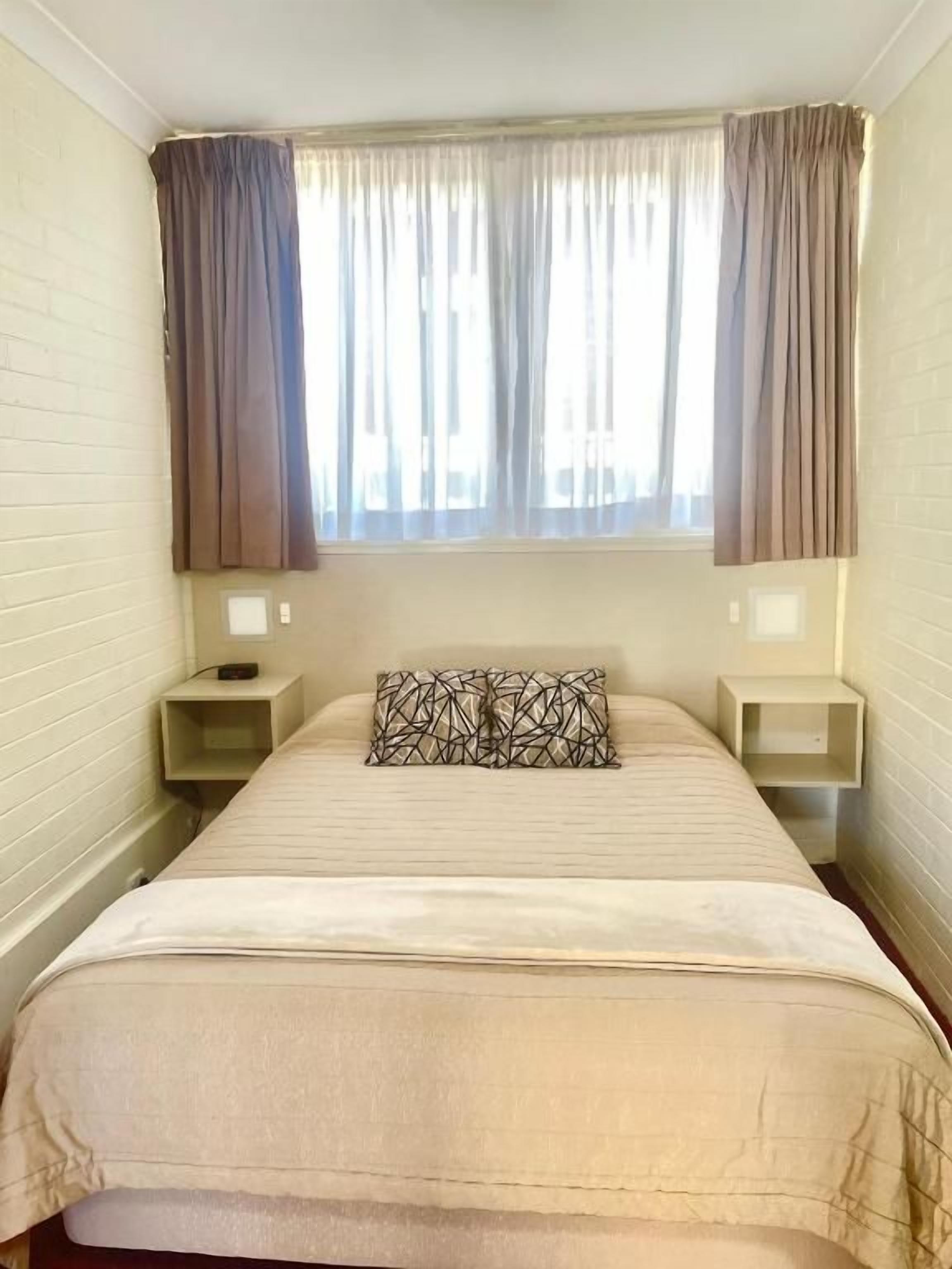 A single bed with a patterned pillow, two bedside tables, and a window with curtains.