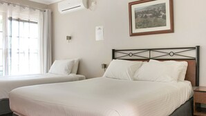 A hotel room with two beds, a framed picture on the wall, an air conditioning unit, and a window with curtains.