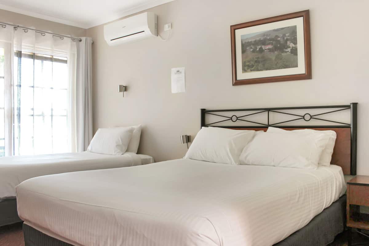 A hotel room with two beds, a framed picture on the wall, an air conditioning unit, and a window with curtains.