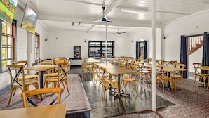 A spacious room with multiple tables and chairs, large windows, and ceiling fans.