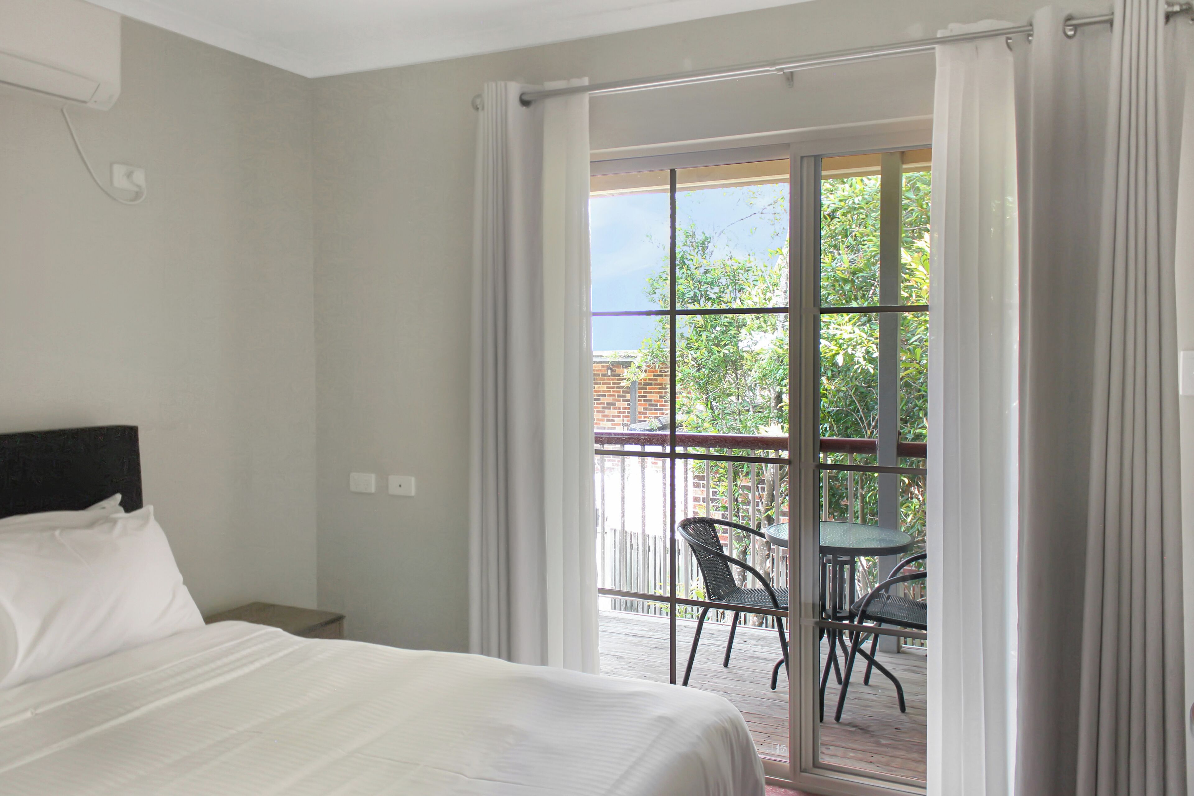 A hotel room with a bed, a small table, and a balcony with chairs.