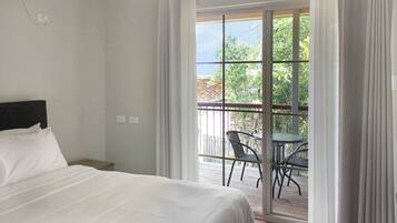 A hotel room with a bed, a small table, and a balcony with chairs.