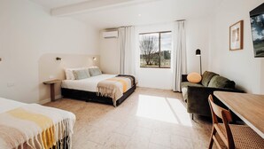 Un dormitorio moderno con cama, sofá, mesa y ventana con cortinas.